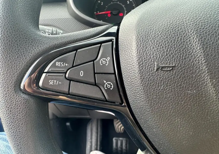 Gros plan sur les commandes du régulateur de vitesse à gauche du volant en cuir d'une Dacia Sandero Stepway bleu foncé 2021.
