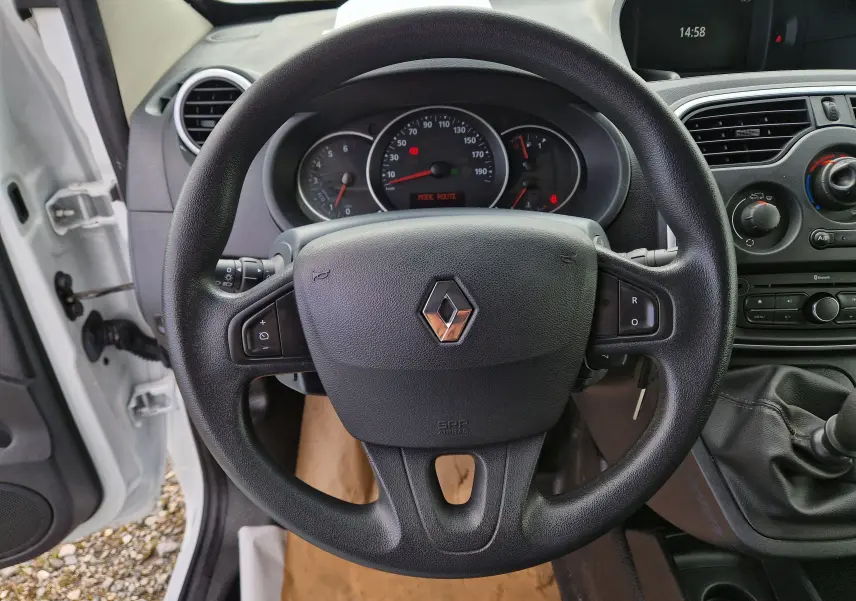 Vue intérieure centrée sur le volant noir d’un Renault Kangoo blanc 2020 avec tableau de bord et levier de vitesses manuel visibles.
