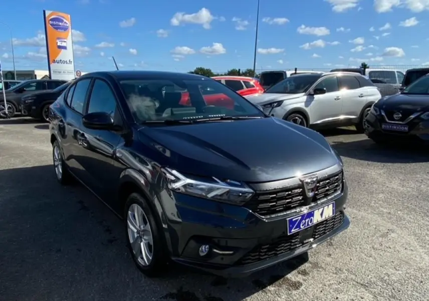 Dacia Logan gris vue 3/4 avant droit sur parking, avec calandre noire et phares LED allumés.