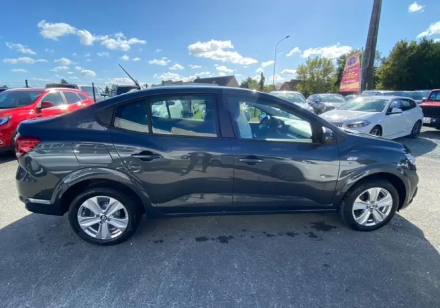 Vue de profil côté gauche d'une Dacia Logan gris métallisé 2022 stationnée en extérieur par temps ensoleillé.