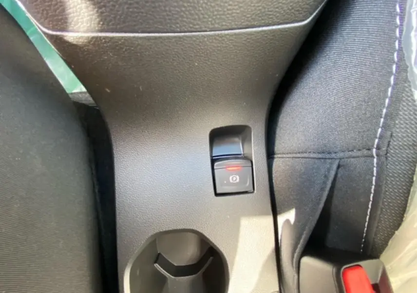 Vue rapprochée du frein à main électrique et porte-gobelet central sur la console d’une Dacia Logan gris 2022.