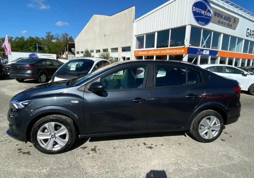 Vue de profil côté gauche d'une Dacia Logan gris foncé 2022 stationnée devant un garage multimarque.