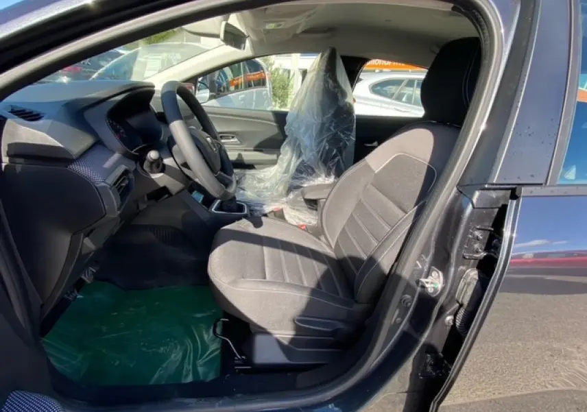Vue intérieure côté conducteur de la Dacia Logan gris 2022, montrant les sièges et le volant avec plastique de protection.