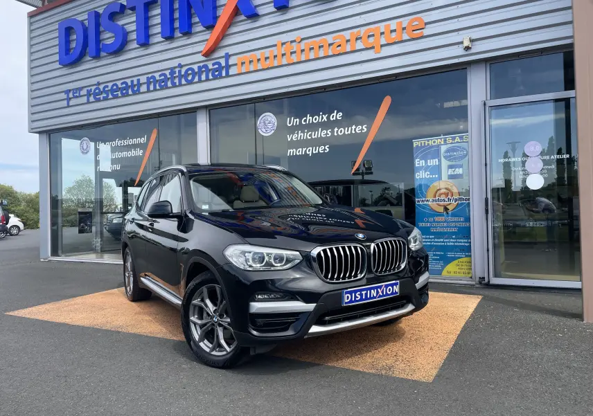 BMW X3 noir vue 3/4 avant droit, garée devant un showroom avec logo Distinxion en arrière-plan.