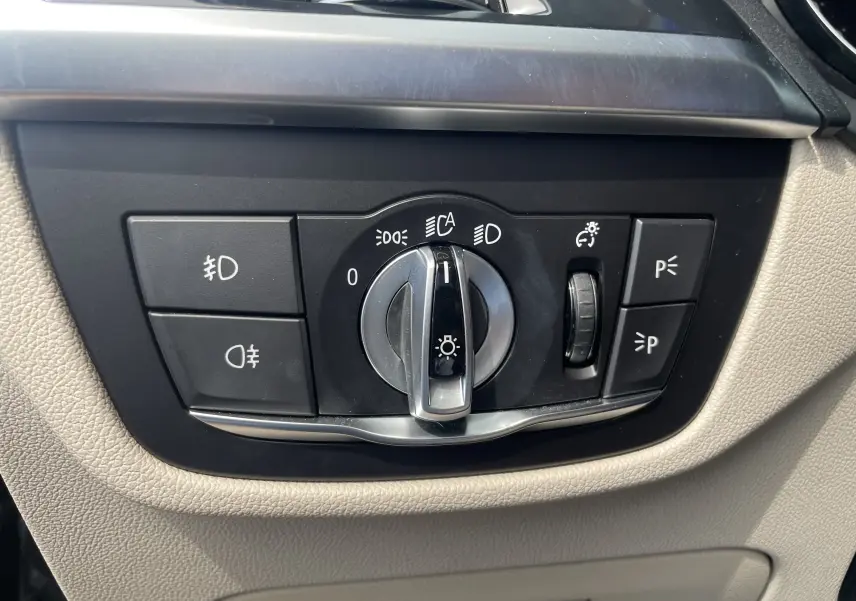 Gros plan sur le bouton de commande des phares dans l’habitacle beige d’un BMW X3 noir (G01) 2021.