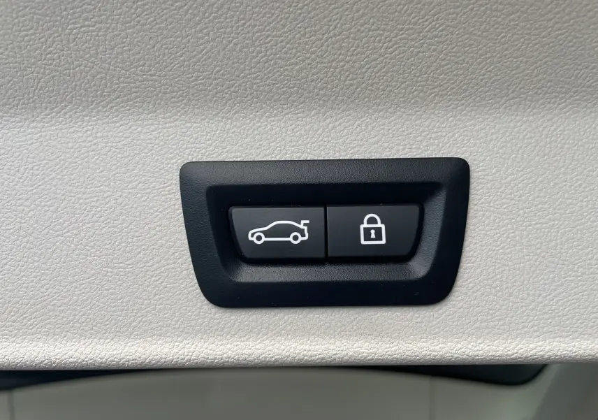 Boutons noirs de commande d'ouverture du coffre et de verrouillage, intégrés dans un panneau intérieur beige clair du BMW X3 noir (G01).