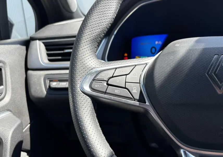 Gros plan sur le volant perforé de la Renault Symbioz noir étoilé, avec commandes intégrées et tableau de bord numérique bleu en arrière-plan.