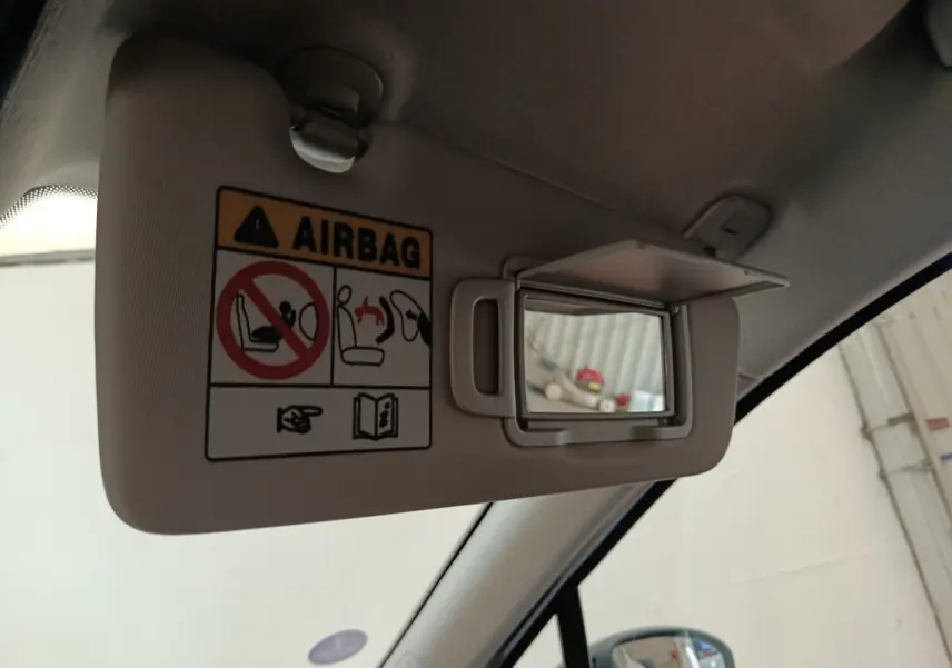 Détail intérieur du pare-soleil côté conducteur avec miroir et avertissement airbag dans une Renault Clio blanche.