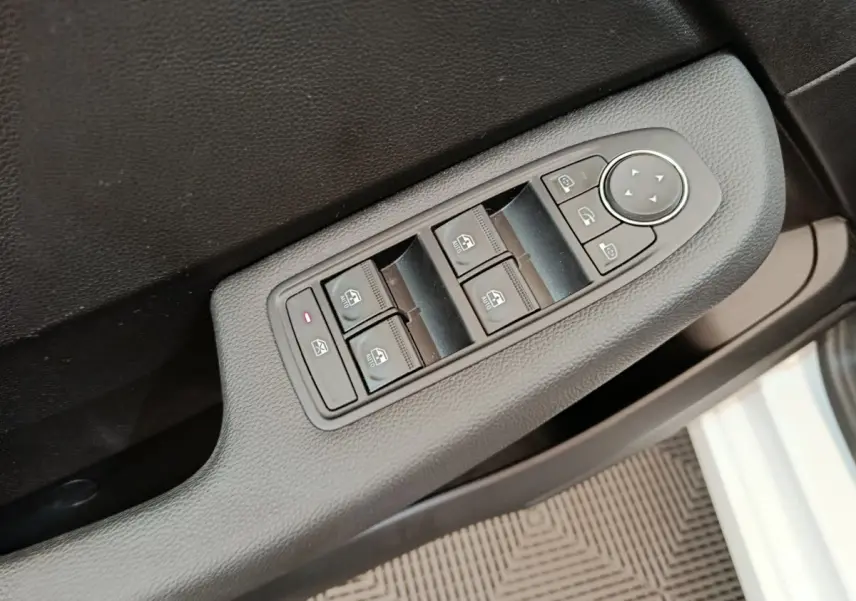 Vue rapprochée des commandes de lève-vitres et rétroviseurs sur la porte côté conducteur d’une Renault Clio blanche 2023.