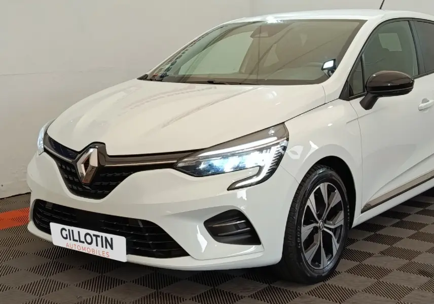 Renault Clio Evolution TCe 90 blanche vue en 3/4 avant droit avec phares LED allumés et jantes alliage noires.