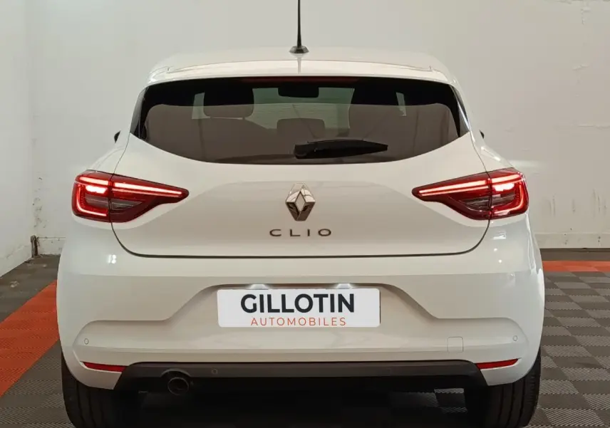 Vue arrière d'une Renault Clio blanche 2023 avec feux LED allumés et logo Renault bien visible.
