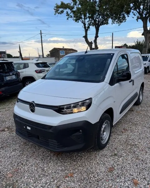 Citroën Berlingo Van Diesel blanc vu en 3/4 avant droit, avec calandre noire et phares allumés sur parking extérieur.