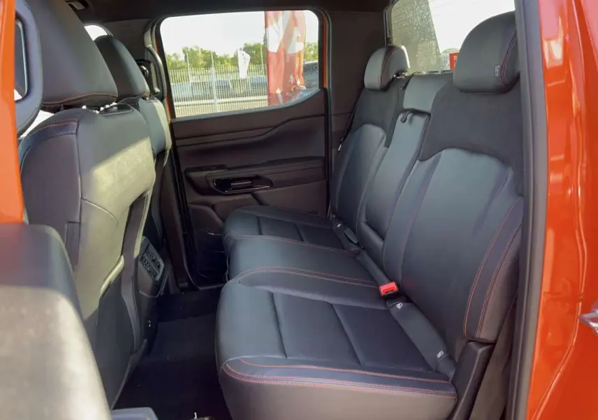 Vue intérieure arrière côté droit du Ford Ranger Wildtrak 2026 orange, sièges cuir noirs avec surpiqûres orange.