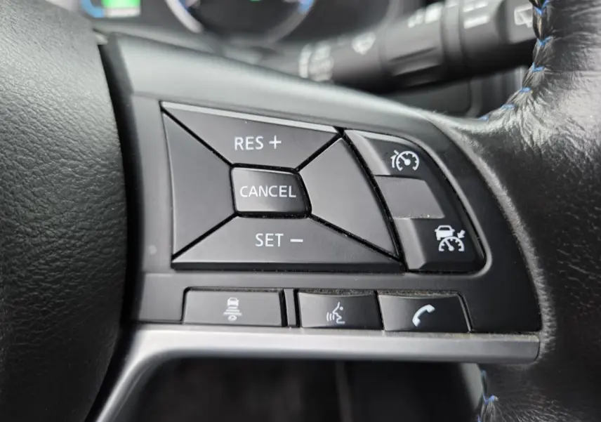 Gros plan sur les commandes du régulateur de vitesse au volant cuir noir d'une Nissan Leaf II gris foncé 2021.