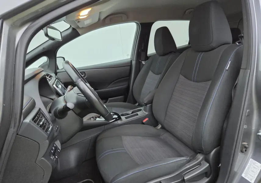 Vue intérieure côté conducteur de la Nissan Leaf II gris foncé, montrant les sièges noirs avec surpiqûres bleues et le volant cuir.