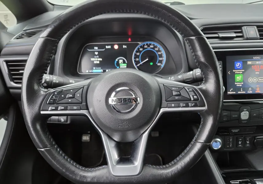 Vue intérieure centrée sur le volant cuir noir de la Nissan Leaf II 150CH avec tableau de bord digital et écran tactile.