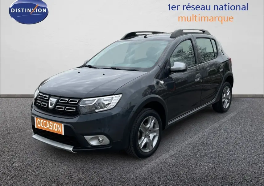 Dacia Sandero Stepway gris foncé vue 3/4 avant droit avec barres de toit et jantes alliage.