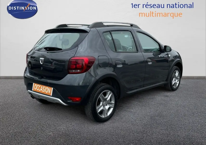 Vue 3/4 arrière droite d'une Dacia Sandero Stepway 0.9 TCe gris foncé de 2016 avec badge Stepway sur la porte.