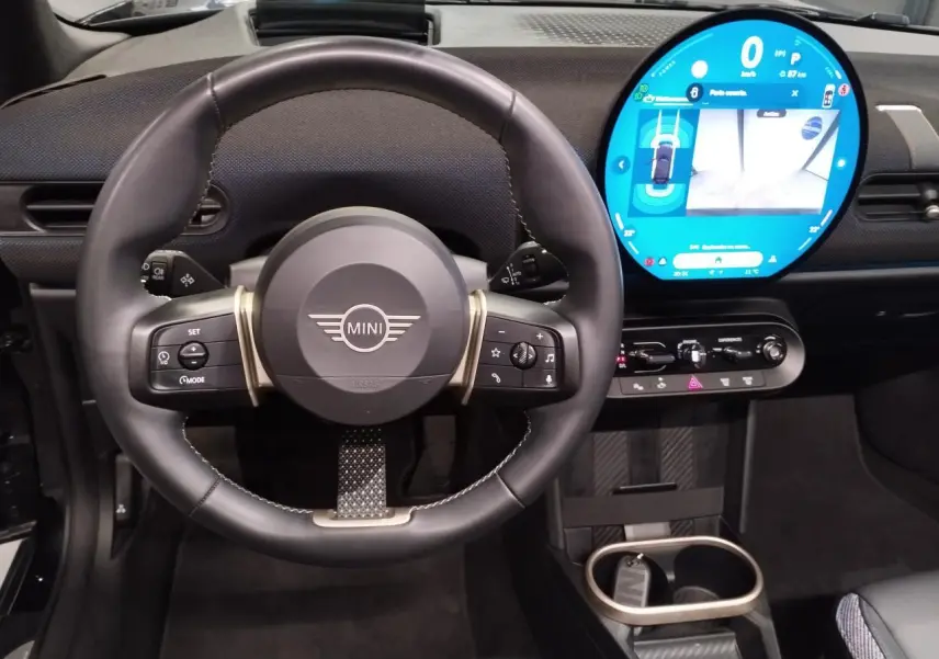 Vue intérieure centrée sur le volant cuir noir et l'écran tactile rond lumineux du tableau de bord MINI Cabriolet 2025.