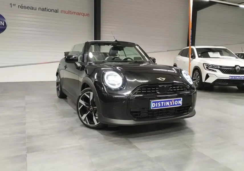 MINI Cabriolet noir vue 3/4 avant droit en intérieur, avec jantes noires à motifs et capote ouverte.