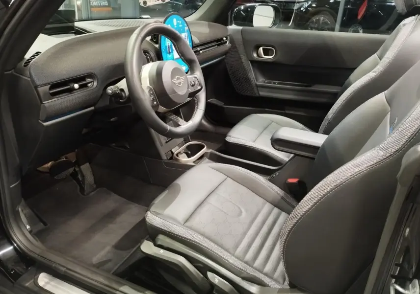 Vue intérieure côté conducteur de la MINI Cabriolet noire 2025, avec sièges sport gris et tableau de bord moderne.