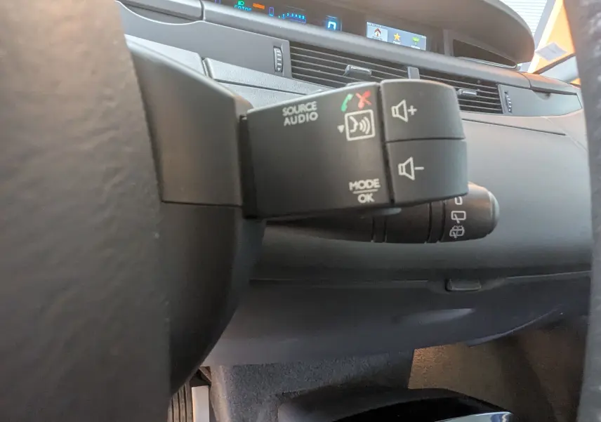 Gros plan sur la commande audio au volant du Renault Grand Espace IV gris clair, avec tableau de bord et écran numérique en arrière-plan.