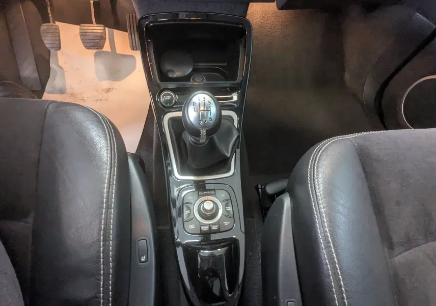 Vue plongeante sur la console centrale noire du Renault Grand Espace IV avec levier de vitesse manuel et sièges en cuir noir.