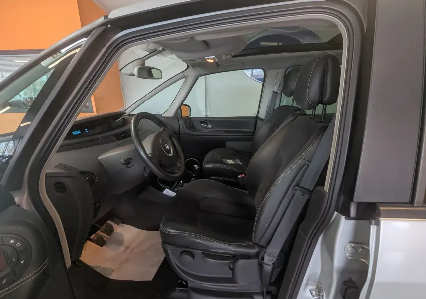 Vue intérieure côté conducteur du Renault Grand Espace IV gris clair de 2012, montrant les sièges noirs en cuir et le volant.