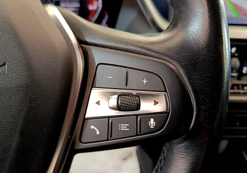 Gros plan sur les commandes du volant côté gauche de la BMW Série 1 118i Edition Sport 2023, cuir noir.