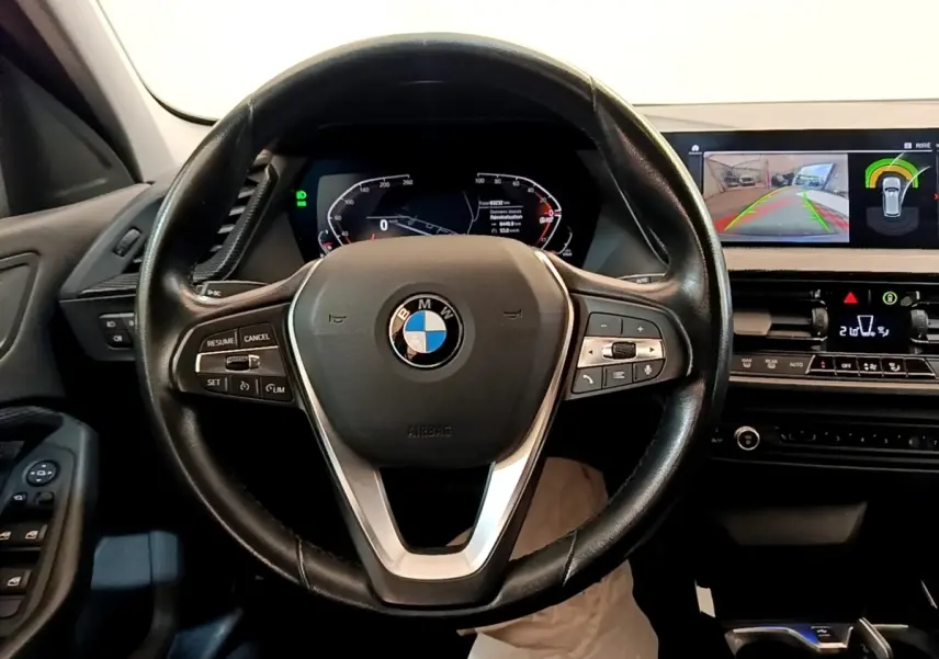 Vue intérieure centrée sur le volant BMW noir et le tableau de bord avec écran tactile affichant la caméra de recul.