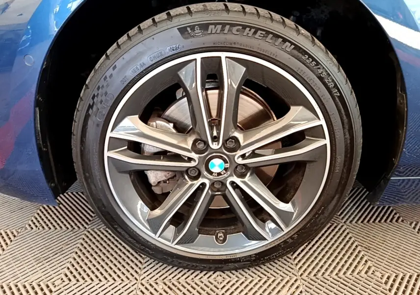 Gros plan sur la roue avant gauche bleu de la BMW Série 1 118i Edition Sport avec jante alliage et pneu Michelin.