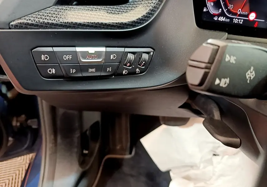 Gros plan sur les commandes d’éclairage et le volant côté gauche de la BMW Série 1 118i bleu 2023.
