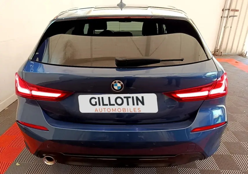 Vue arrière d'une BMW Série 1 118i Edition Sport bleu, feux LED allumés et sortie d'échappement visible côté gauche.