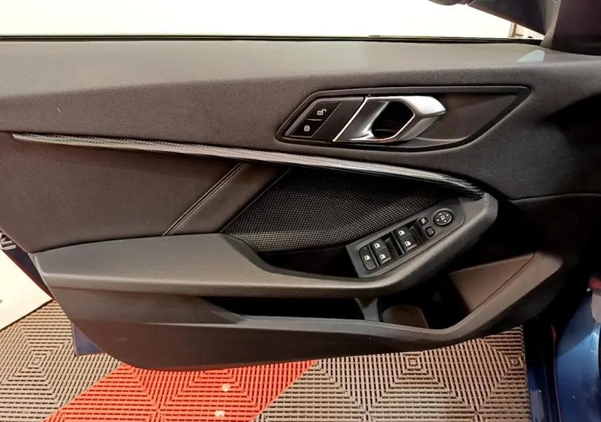 Gros plan sur la porte avant gauche de la BMW Série 1 bleu, montrant la poignée intérieure et les commandes des vitres.