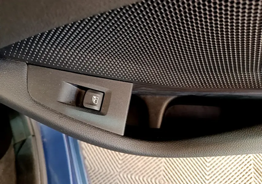 Gros plan sur le bouton de commande de la vitre électrique côté conducteur, avec la porte bleu foncé visible en arrière-plan.
