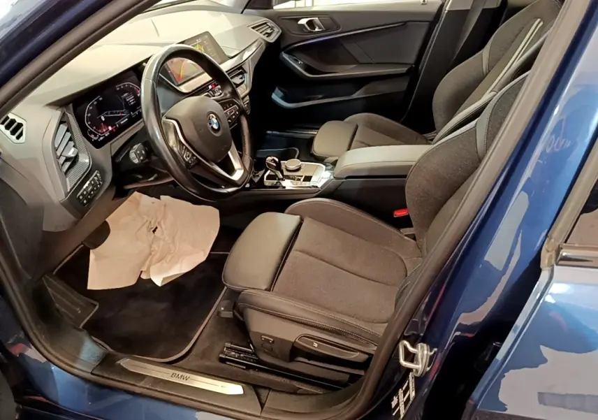 Vue intérieure côté conducteur de la BMW Série 1 118i Edition Sport bleue, avec tableau de bord et sièges noirs.