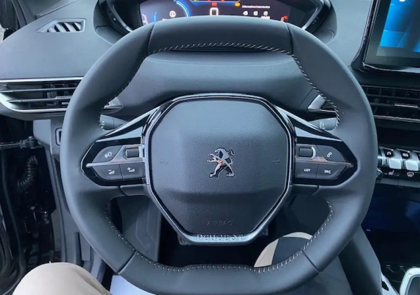 Vue rapprochée du volant noir du Peugeot 5008 2023 avec commandes intégrées et tableau de bord numérique en arrière-plan.