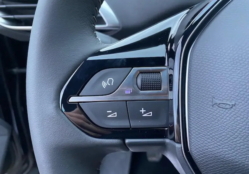 Gros plan sur les commandes gauche du volant noir du Peugeot 5008 2023, avec boutons de volume et reconnaissance vocale.