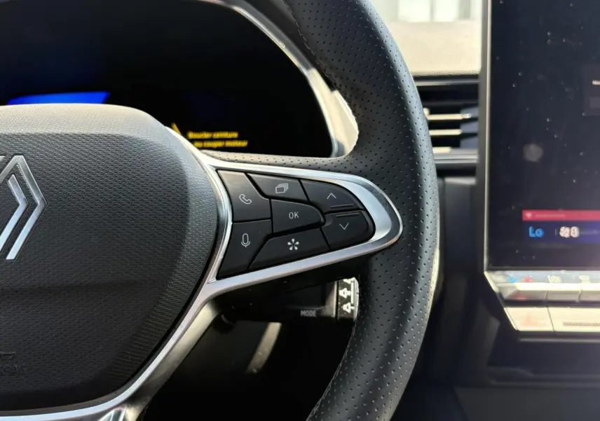 Gros plan sur le côté droit du volant perforé noir avec commandes intégrées et écran tactile du tableau de bord Renault Symbioz.
