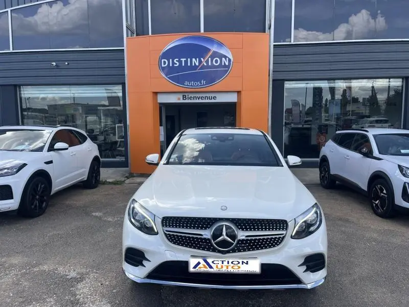 Vue avant d'une Mercedes GLC Coupé 220 d blanc diamant brillant designo, calandre AMG et phares LED allumés.