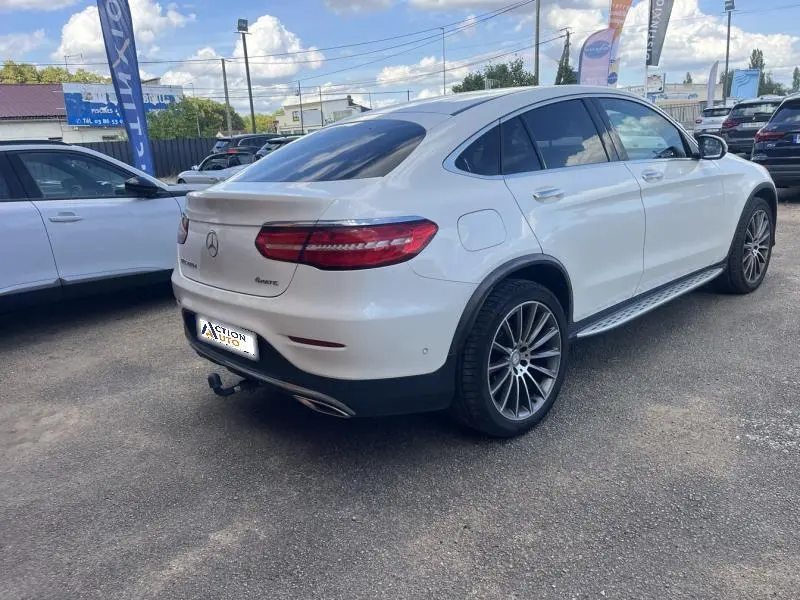 Vue 3/4 arrière droite d'un Mercedes GLC Coupé blanc diamant brillant avec jantes AMG multibranches bicolores.