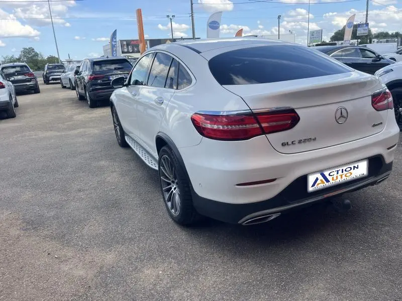 Vue 3/4 arrière droite d'un Mercedes GLC Coupé blanc diamant brillant avec jantes AMG multibranches bicolores et vitres surteintées.