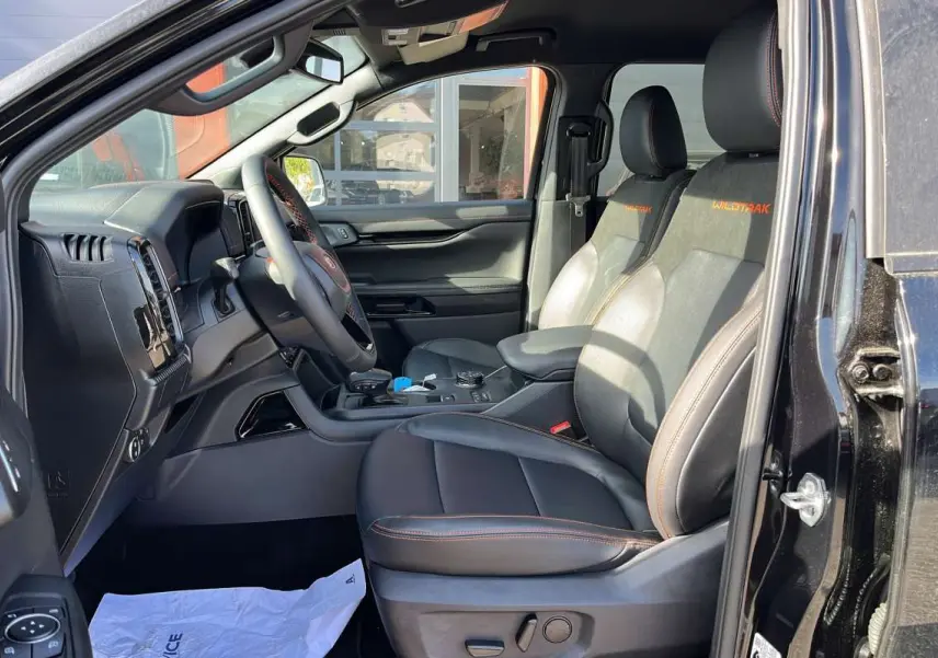 Vue intérieure côté conducteur du Ford Ranger Wildtrak 2026 noir agate, sièges cuir avec surpiqûres orange et console centrale moderne.