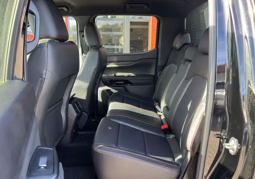 Vue intérieure côté droit sur la banquette arrière en cuir noir avec surpiqûres orange du Ford Ranger Wildtrak Plus noir agate.