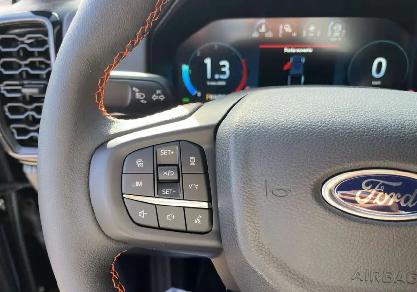 Gros plan sur le volant cuir noir avec surpiqûres orange du Ford Ranger Wildtrak 2026, affichage numérique en arrière-plan.