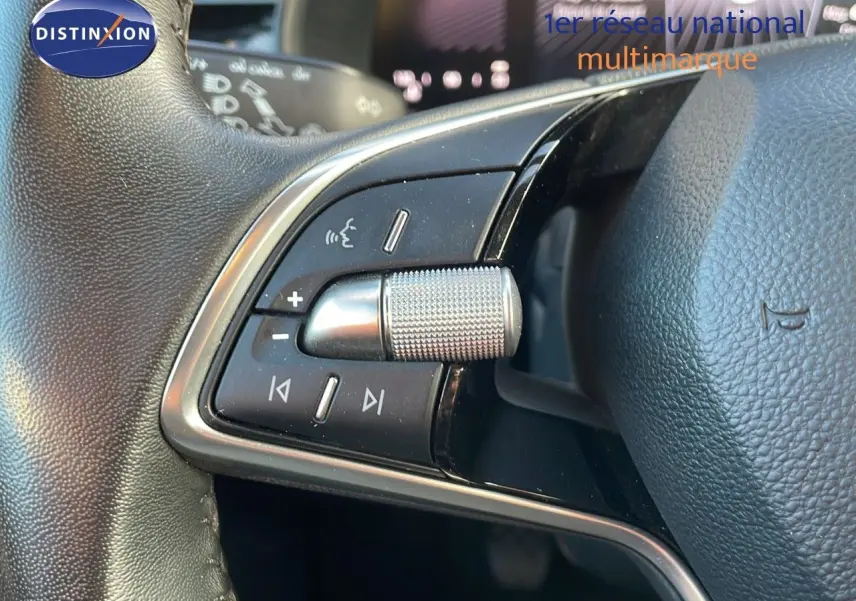 Gros plan sur les commandes audio au volant d'un Skoda Kamiq gris graphite, mettant en valeur la molette métallique texturée.