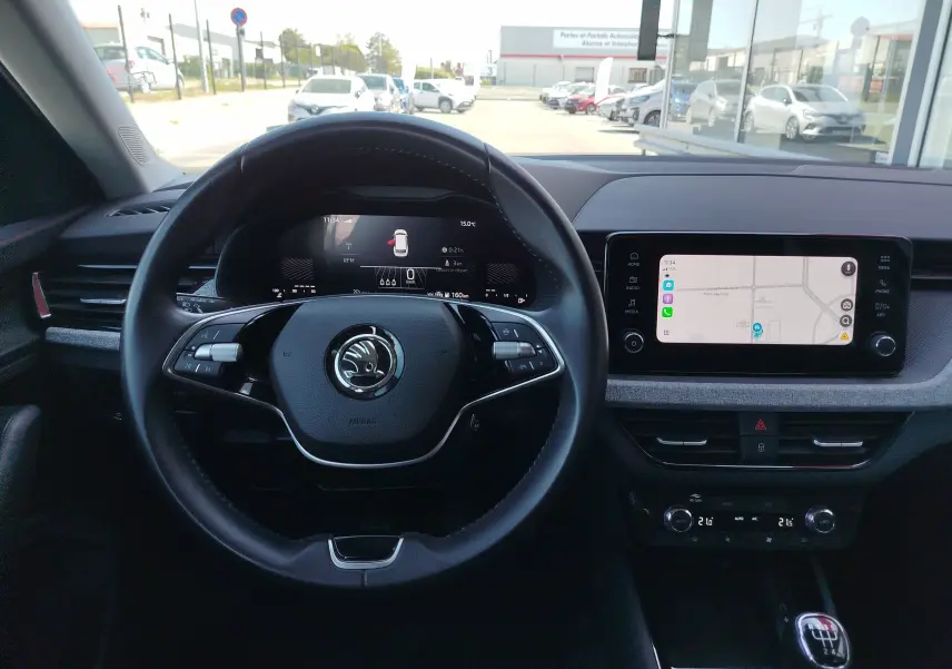 Vue intérieure centrée sur le volant et le tableau de bord numérique d'une Skoda Kamiq 2024, avec écran tactile et levier de vitesses manuel.