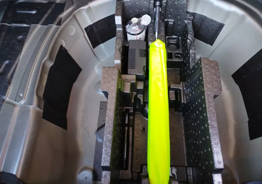 Vue plongeante sur le rangement sous le coffre d'un Skoda Kamiq 2024, avec un gilet jaune et une bouteille d'eau.