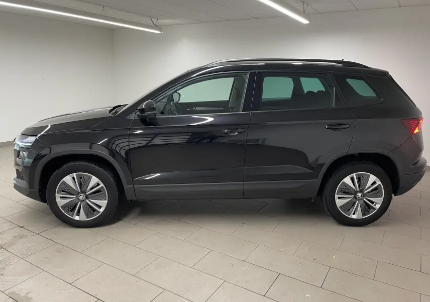 Profil côté gauche du SUV SKODA KAROQ 2023 en noir Magic nacré, avec jantes modernes et feux arrière allumés.