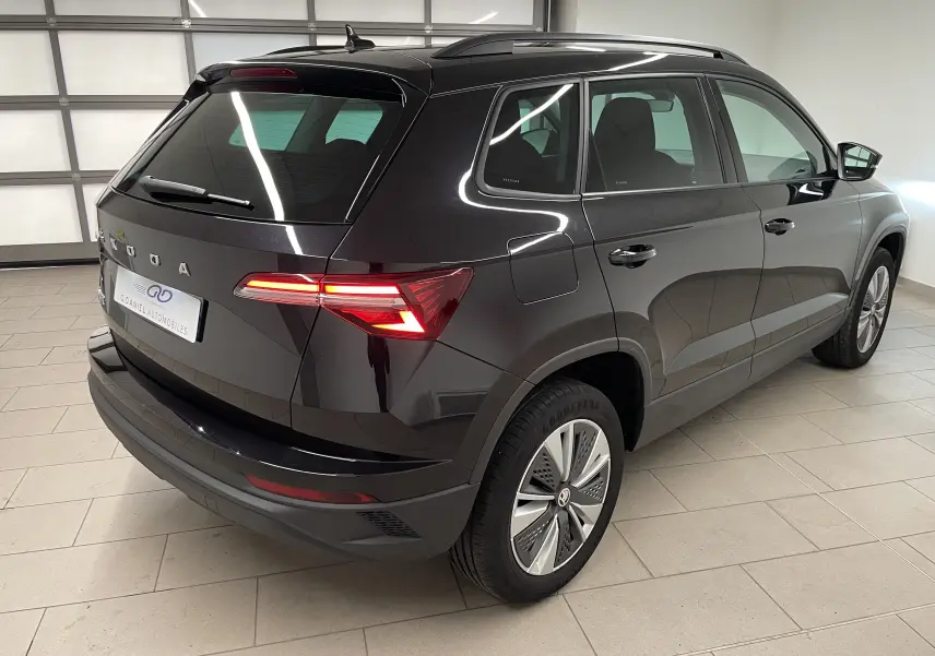 Vue 3/4 arrière droite du SUV SKODA KAROQ noir Magic nacré avec feux arrière allumés dans un garage lumineux.